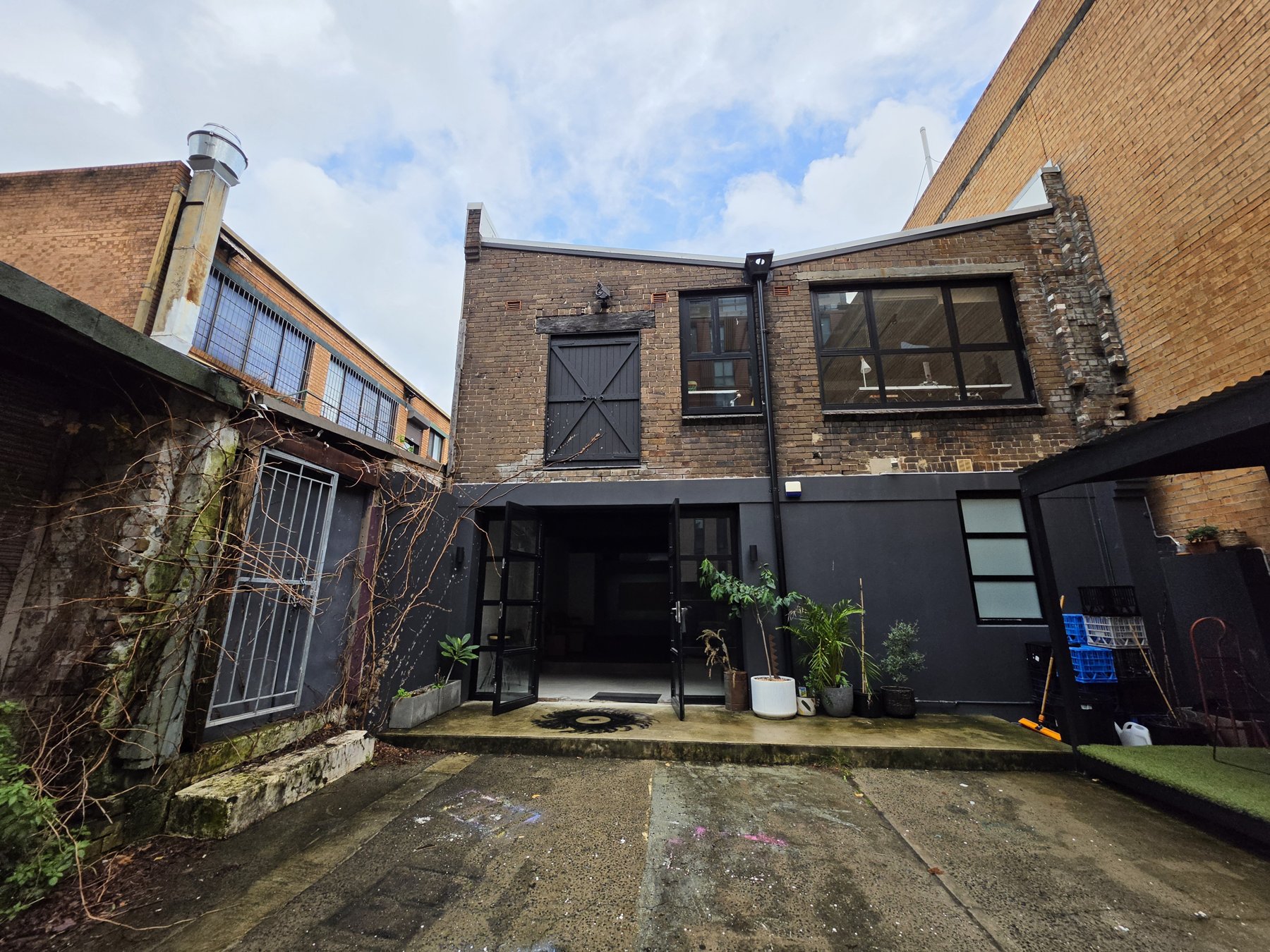 The full courtyard — heritage brick facade, plants at the door.