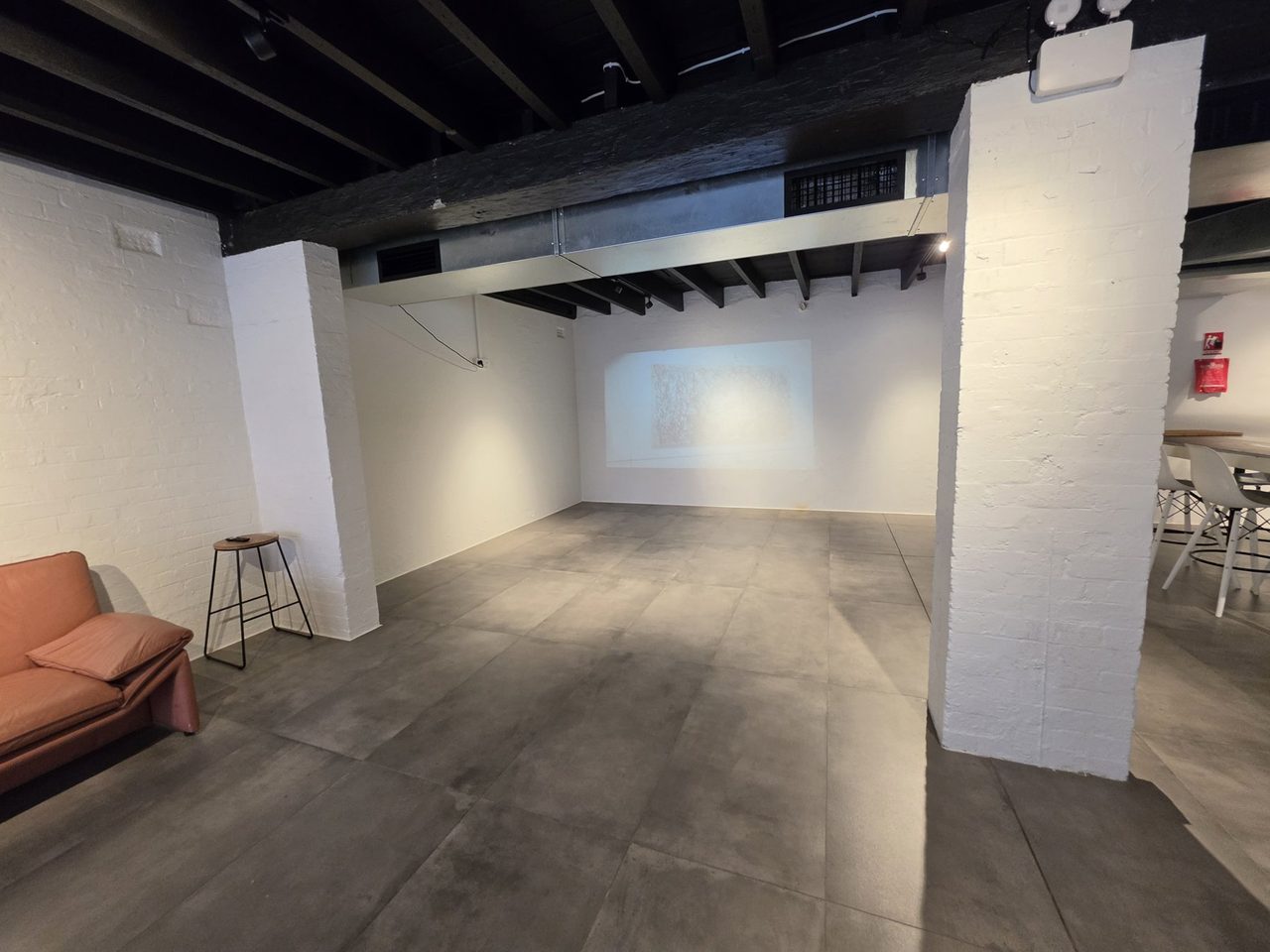 Projector wall and the terracotta sofa corner, steel beams overhead.