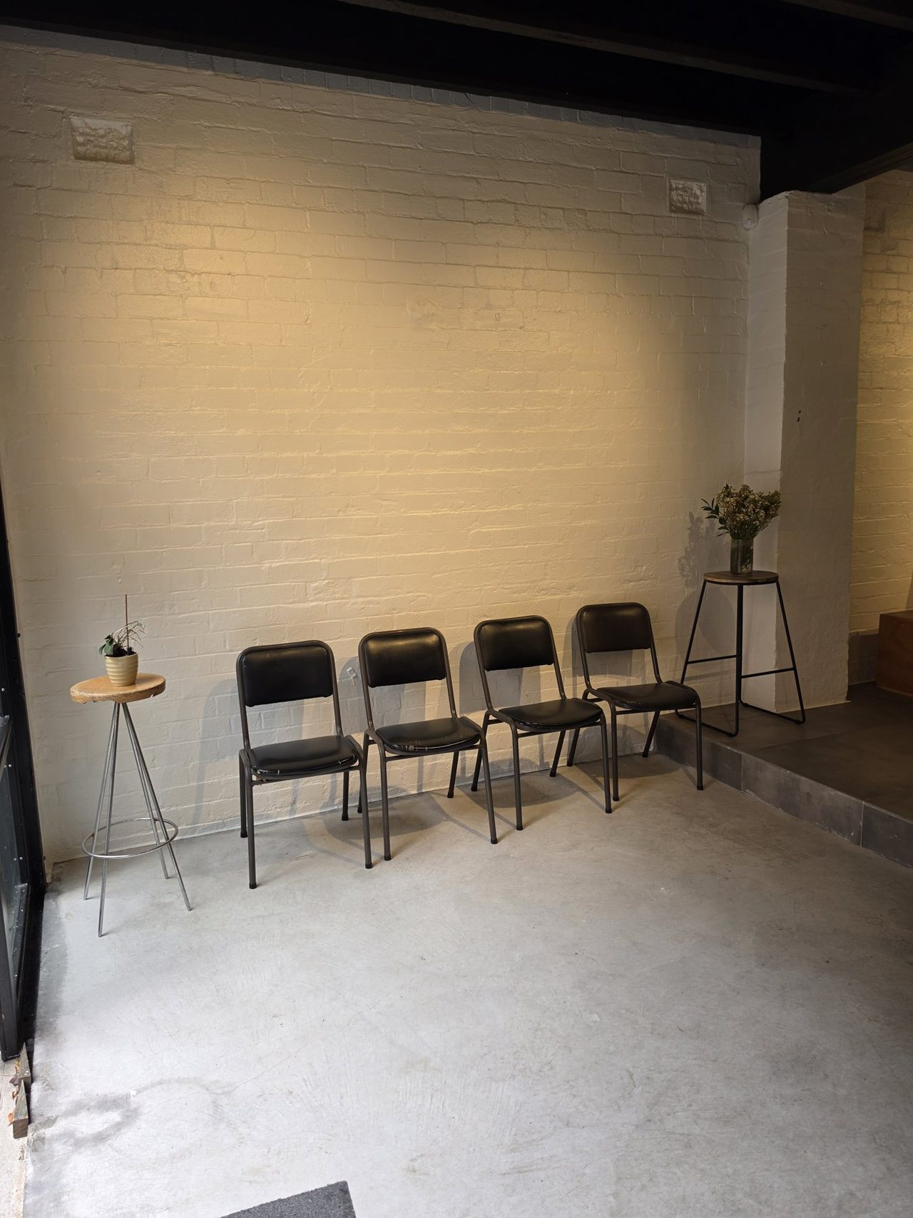 Chairs in a row against white brick, side table with flowers.