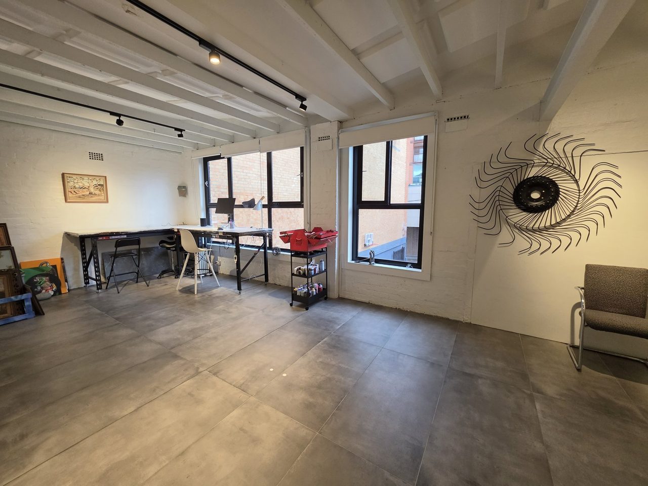 The loft floor full length — work tables, tall windows, sunburst sculpture.