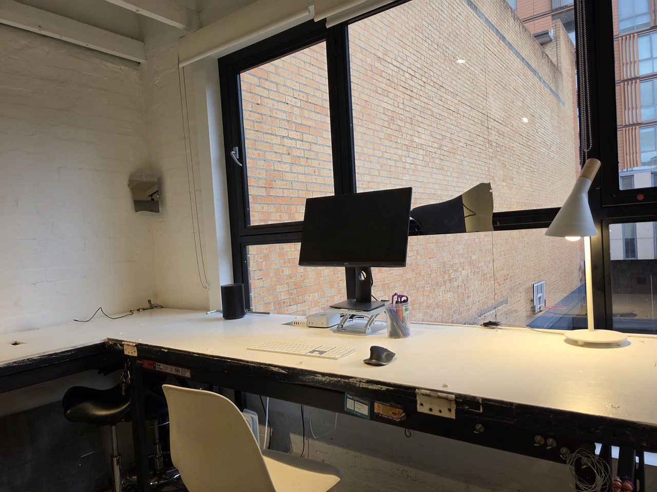 A window desk with monitor and lamp, brick wall opposite.