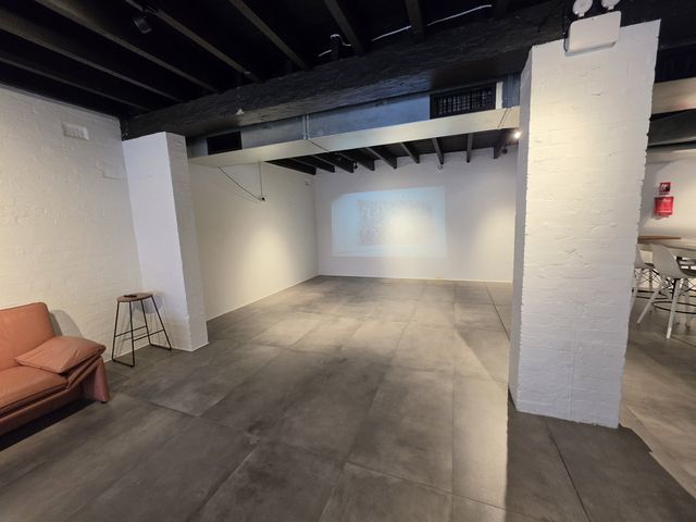 Projector wall and the terracotta sofa corner, steel beams overhead.